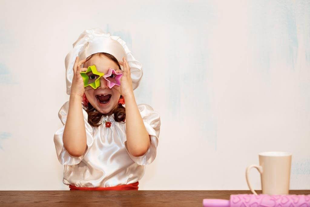 Весела дівчинка у костюмі кухаря грається формочками для печива у вигляді зірок