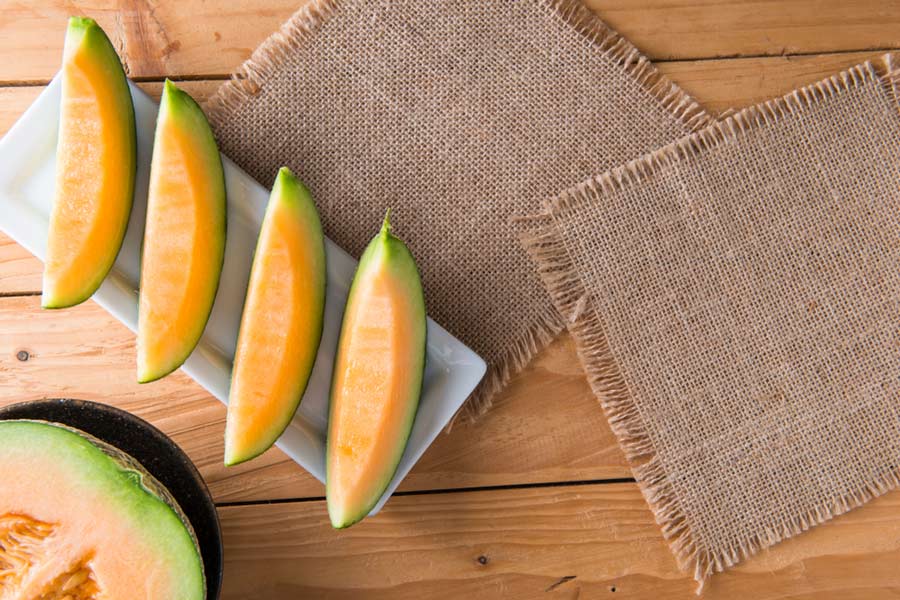 Нарізані скибочки помаранчевої дині на білій тарілці на дерев'яному столі