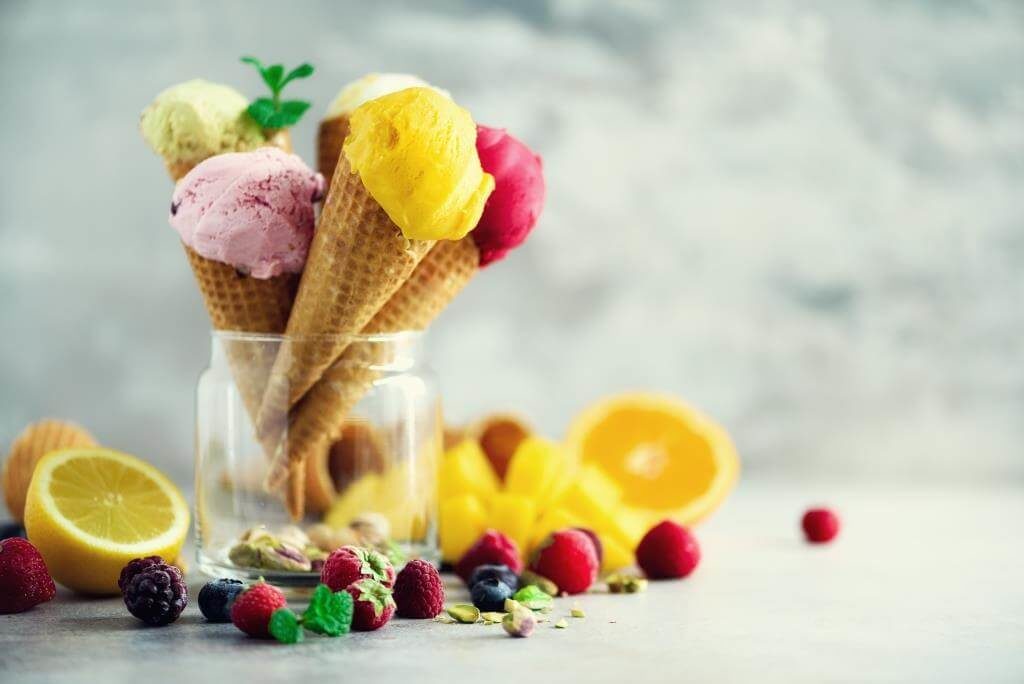 Кілька різнокольорових кульок морозива у вафельних ріжках, прикрашених фруктами