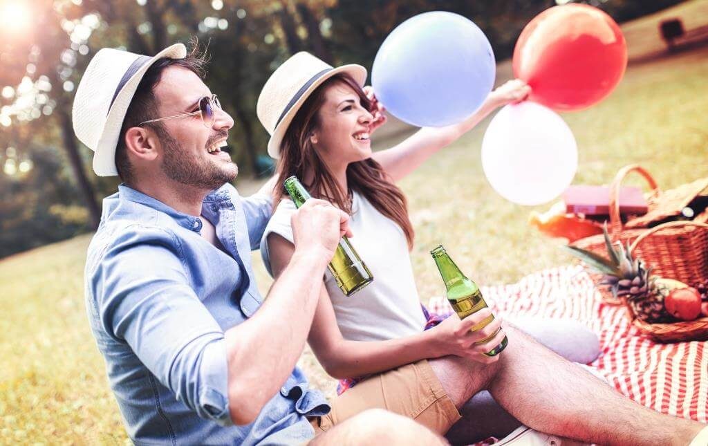 Молоді люди на пікніку з напоями та повітряними кульками в парку