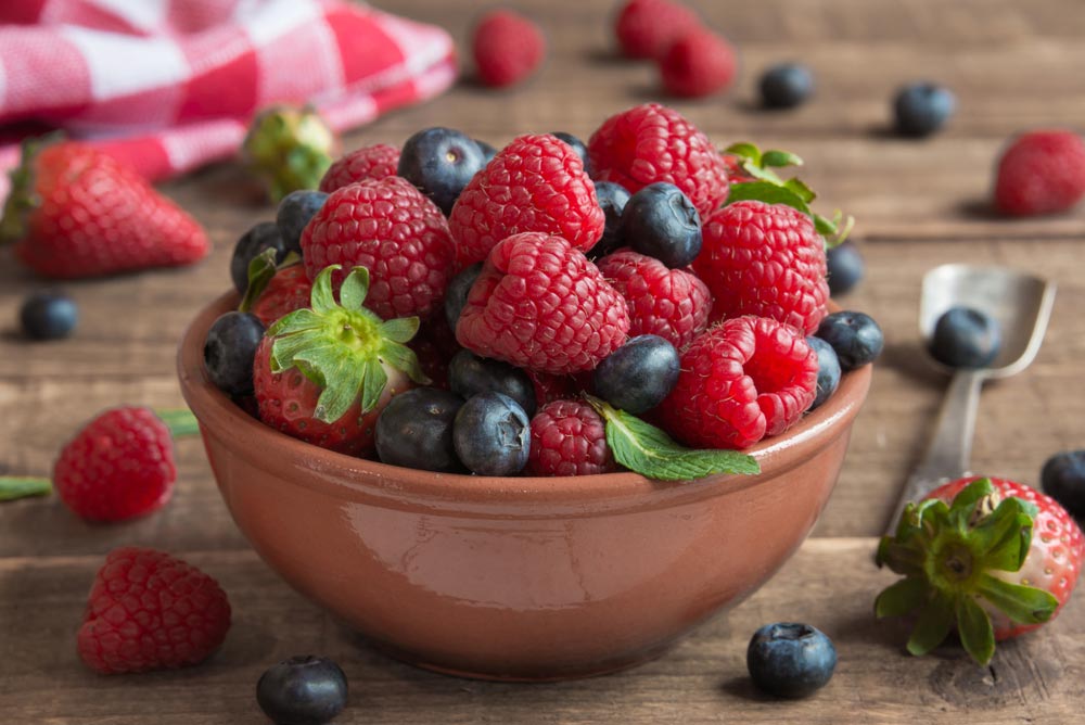 Миска зі свіжою малиною, полуницею, чорницею та м’ятою на дерев’яному столі