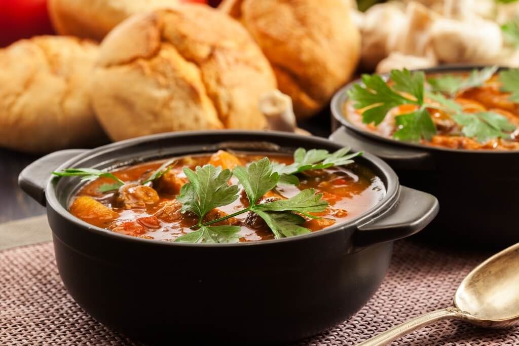 Густий овочевий суп з м’ясом і зеленню в чорній керамічній мисці