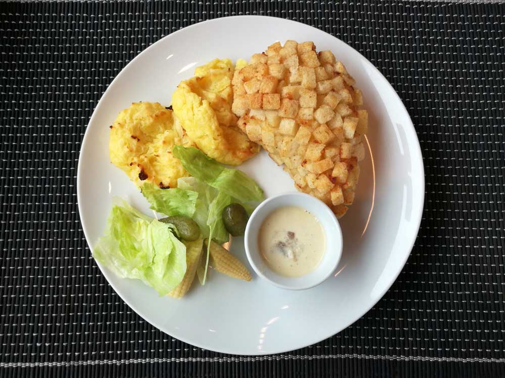 Куряча котлета в картопляній паніровці з пюре, овочами та соусом на тарілці