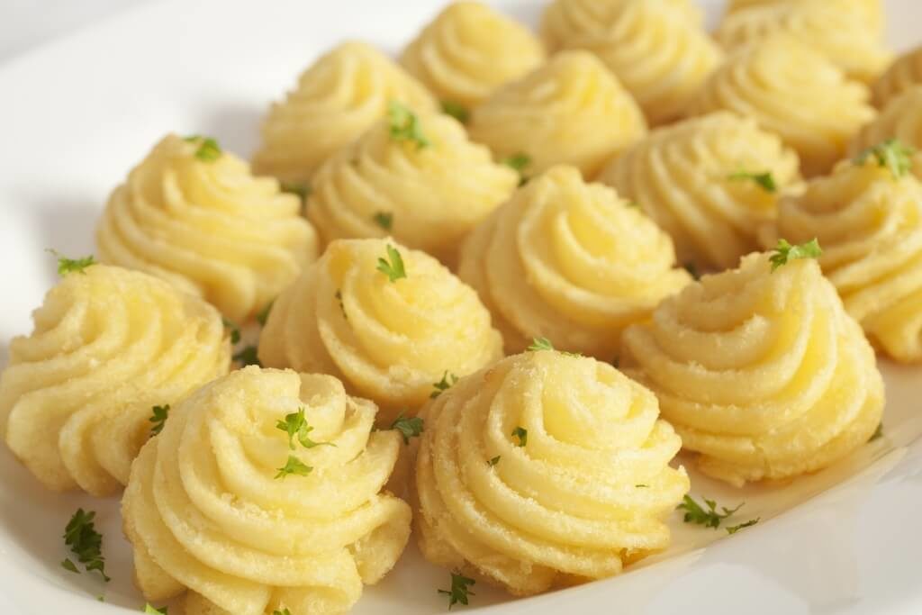 Картопляне пюре, сформоване у вигляді троянд, прикрашене зеленню.