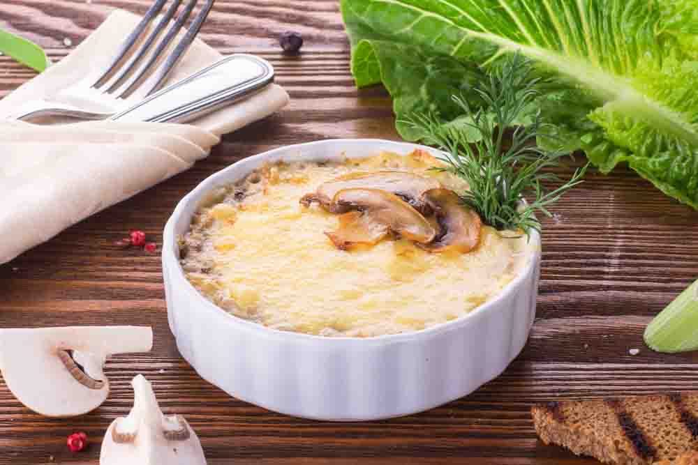 Жульєн з грибами під сирною скоринкою в білій керамічній формі, прикрашений зеленню