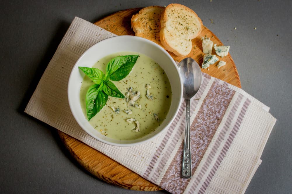 Зелений крем-суп із базиліком і сиром у білому посуді з грінками на серветці