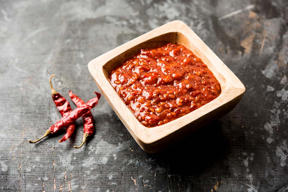 Гострий соус чилі в дерев’яній піалці з сушеними перцями на чорному фоні
