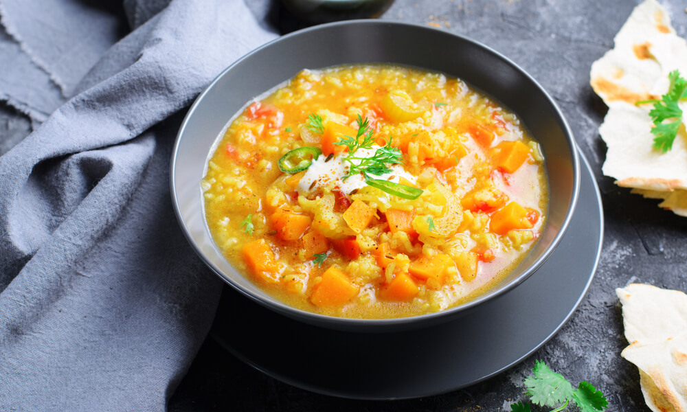 Гарбузовий суп з сочевицею, перцем чилі та зеленню у чорній тарілці, поруч лаваш і серветка.