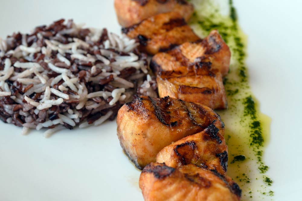 Грильовані шматочки лосося з сумішшю дикого і білого рису, подані з зеленим соусом на білій тарілці