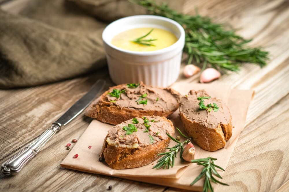 Кусочки багета, намазані печінковим паштетом і посипані зеленню, з розмарином, часником та соусом у білій піалі