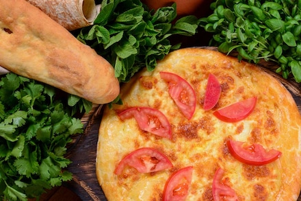 Грузинська хачапурі з томатами, оточена свіжою зеленню та лавашем