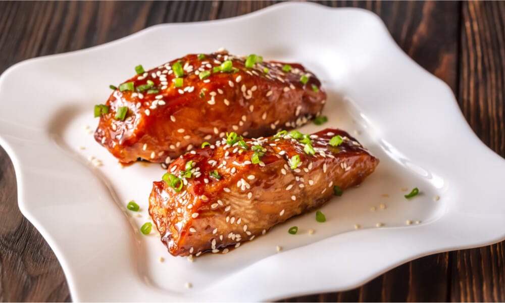 Соковиті шматочки лосося в глазурі з кунжутом та зеленою цибулею на білій тарілці