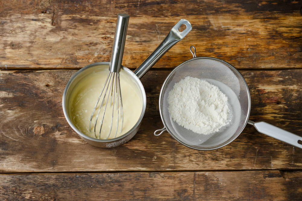 Приготування крему: вінчик у каструлі з масою та сито з борошном.