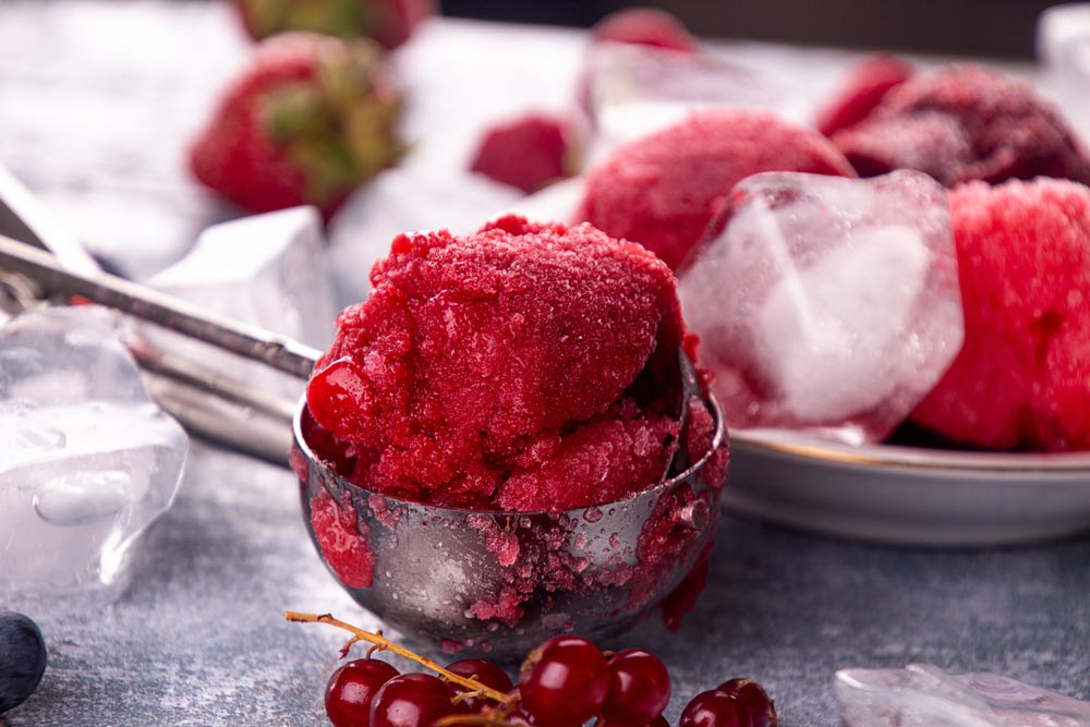 Домашній ягідний сорбет із червоної смородини у металевій ложці на фоні льоду