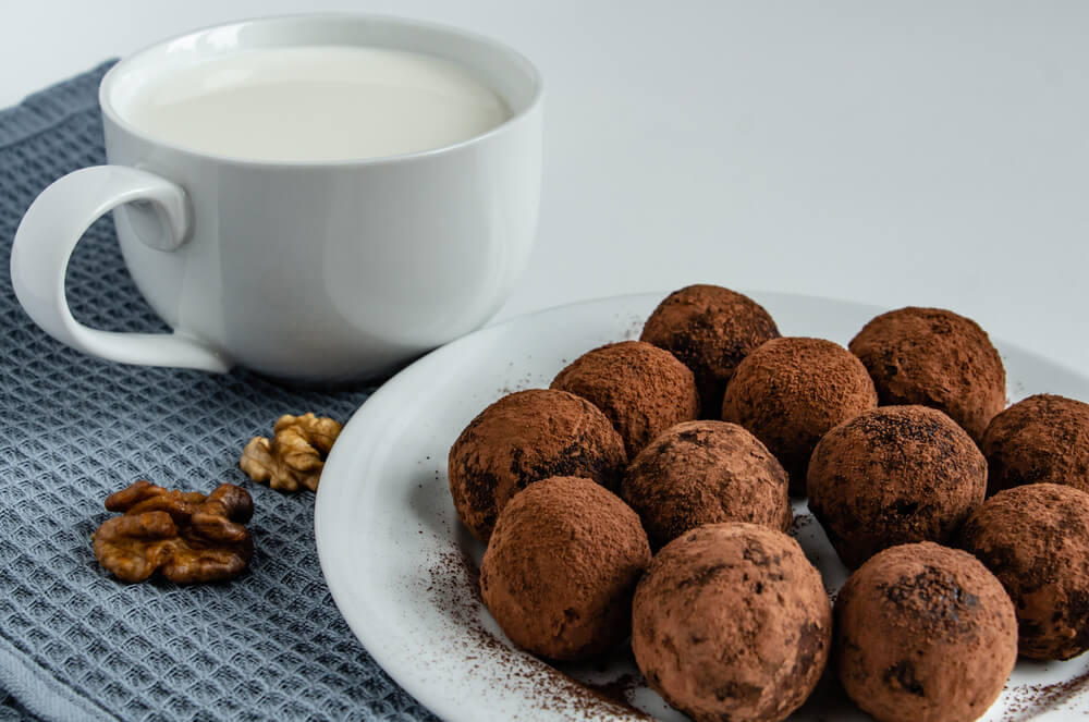 Домашні шоколадні трюфелі в какао на тарілці поруч із чашкою молока та волоськими горіхами