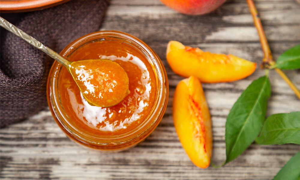 Персиковий джем у скляній банці з ложкою