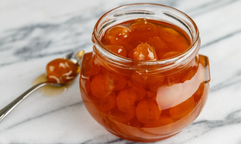 Варення з аґрусу у скляній банці на мармуровій поверхні