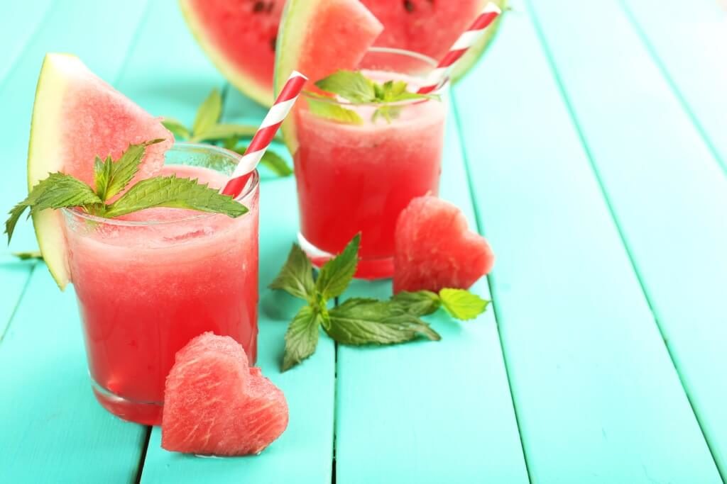 Літній арбузний коктейль із м’ятою, долькою кавуна та трубочкою на бірюзовому фоні