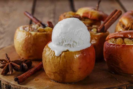 Запечене яблуко з кулькою ванільного морозива, корицею та анісом на дерев’яній підставці.