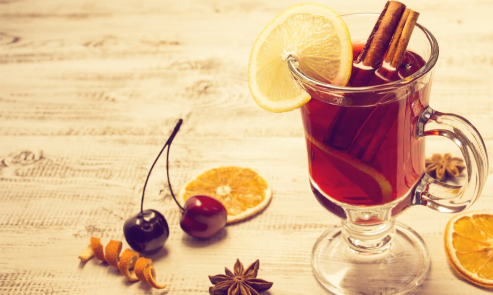 Глінтвейн у склянці з ручкою, прикрашений лимоном і корицею, на білому дерев’яному столі