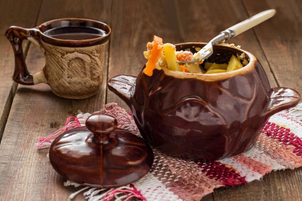 Картопля з овочами, запечена в горщику з глиняним кухлем поруч
