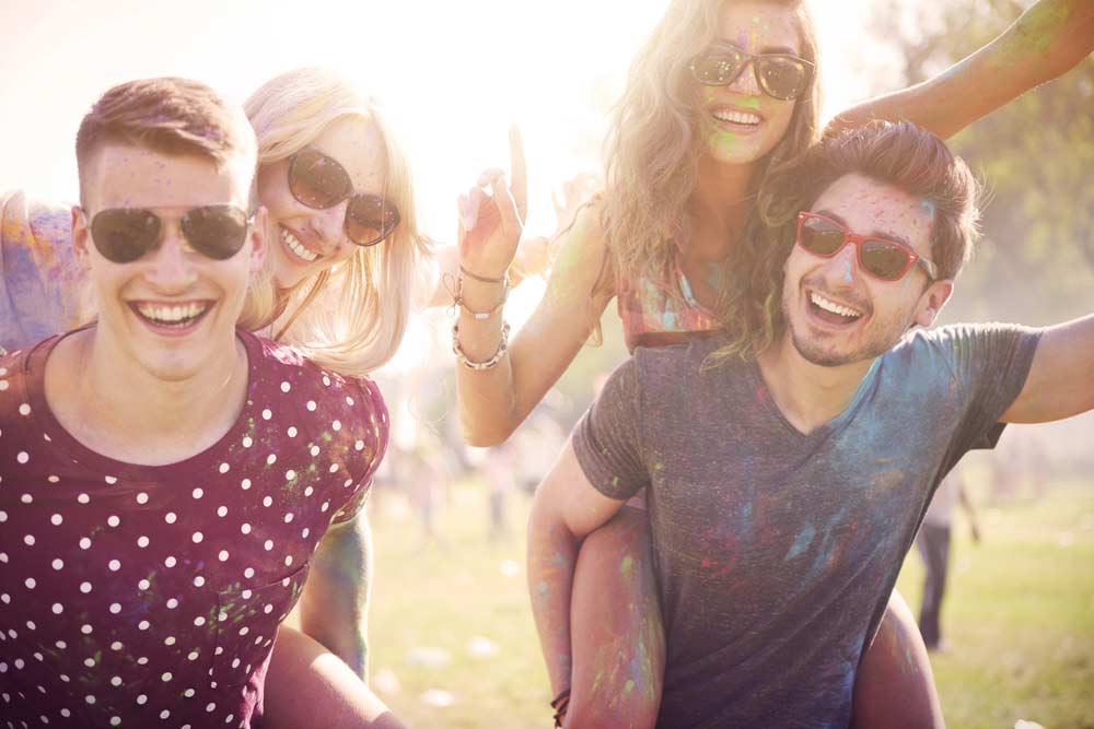 Весела компанія молодих людей на фестивалі фарб Холі, усі усміхаються та розфарбовані