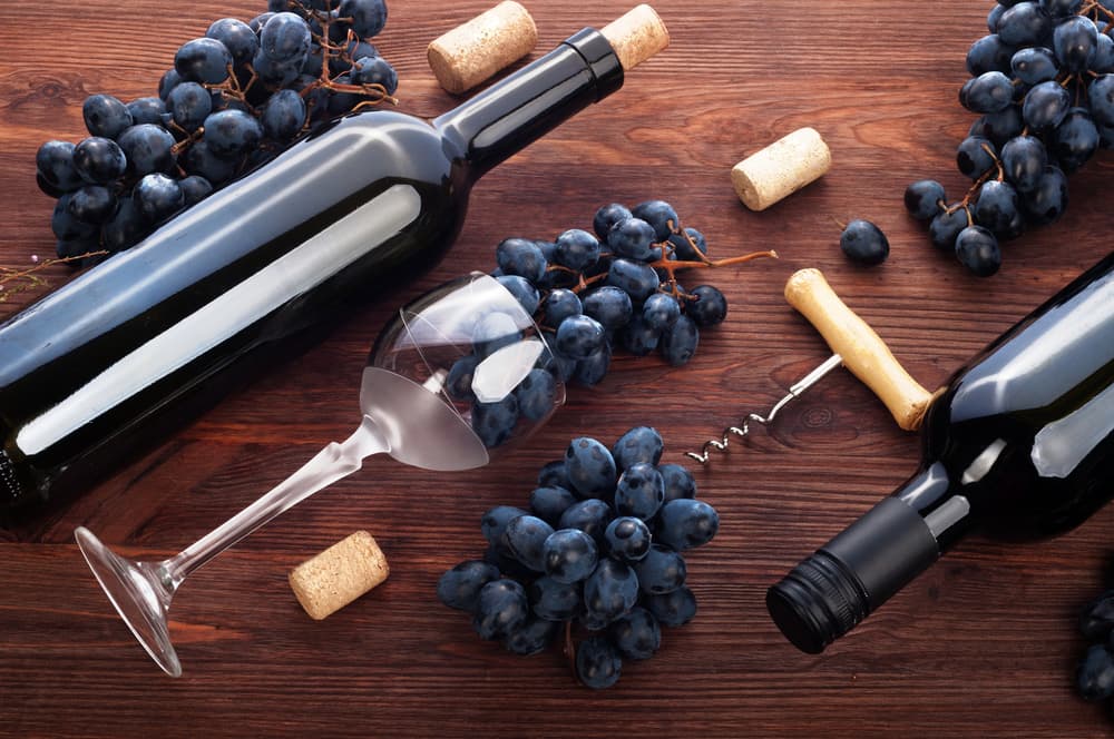 Дерев'яний стіл з пляшками червоного вина, виноградом, келихом та штопором.