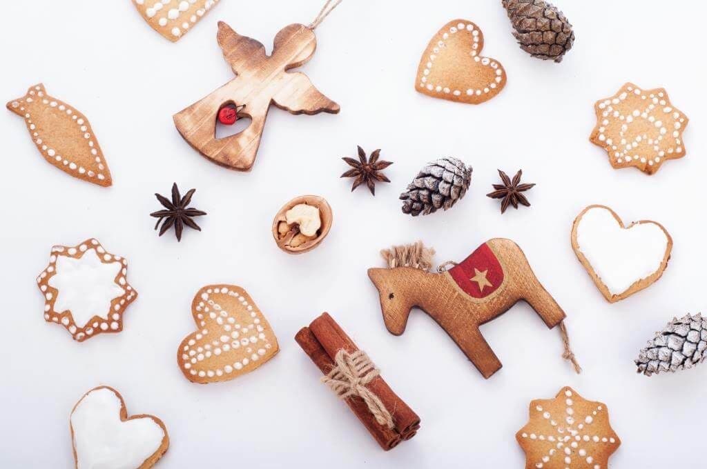 Новорічна композиція з імбирними пряниками, дерев’яними прикрасами та корицею на білому фоні