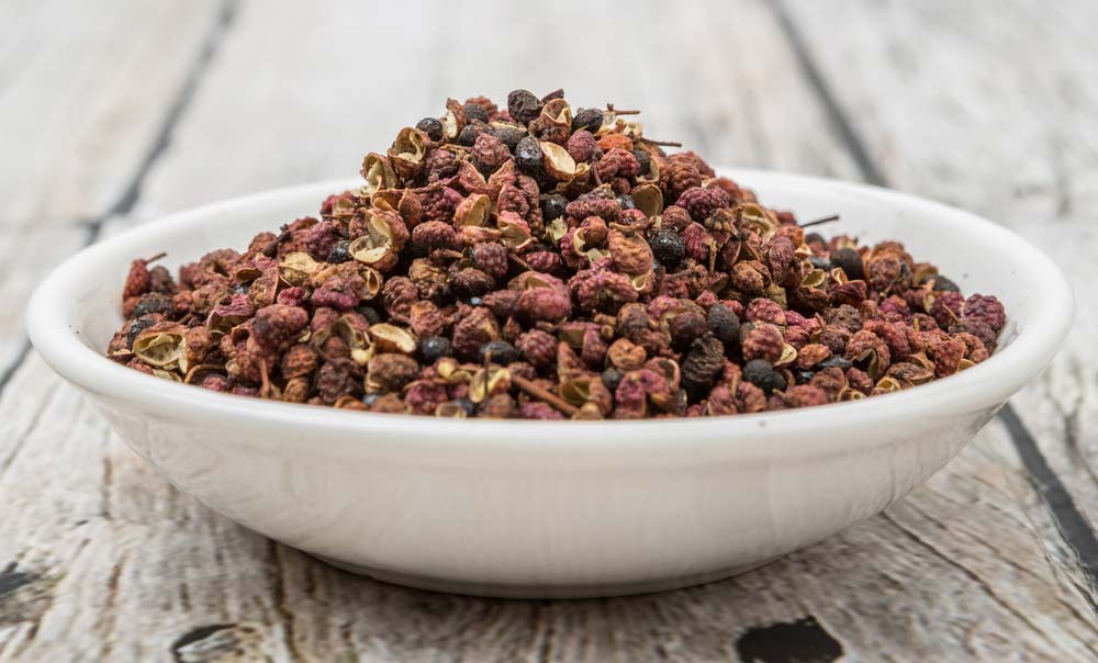 Сушений сичуанський перець у керамічній мисці на дерев’яному фоні