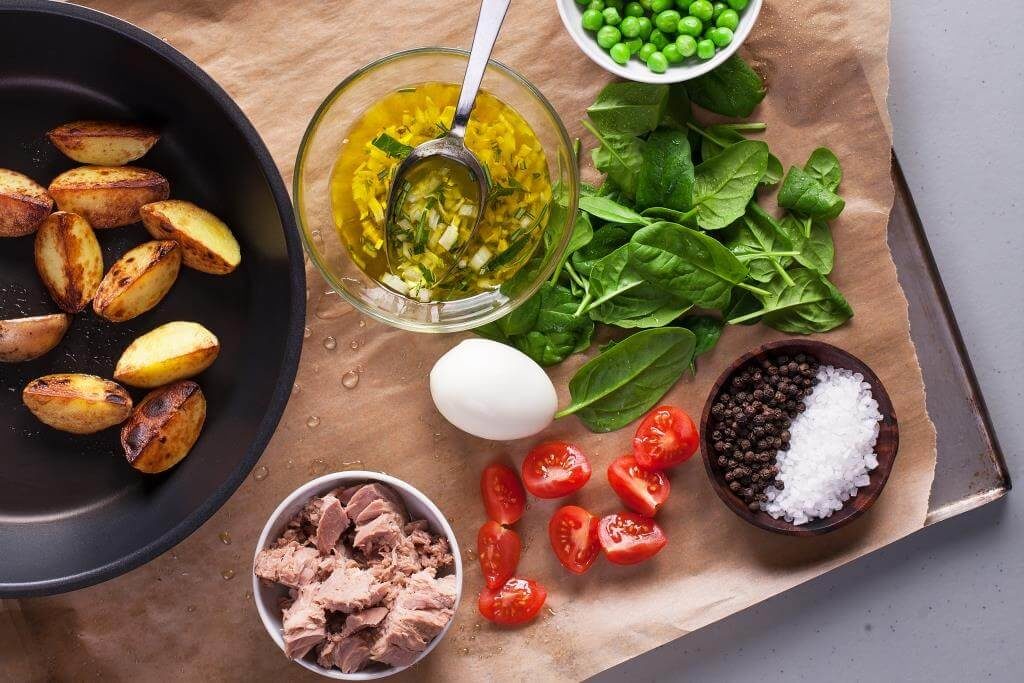 Інгредієнти для салату: обсмажена картопля, тунець, шпинат, яйце, томати, горошок, спеції та заправка в мисці