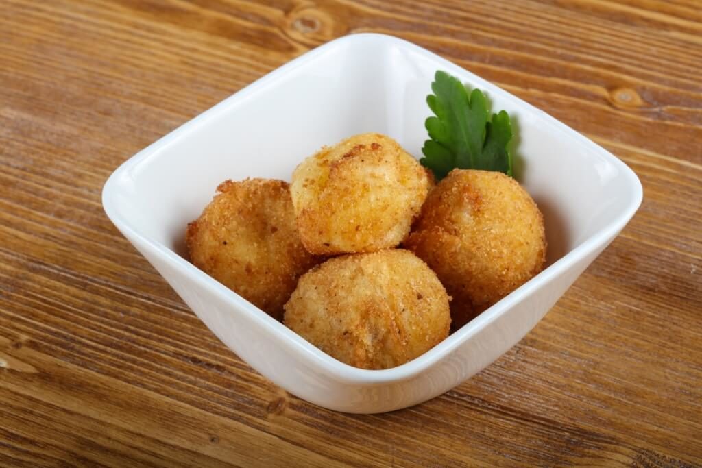 Картопляні крокети в білій квадратній мисці з листком петрушки.
