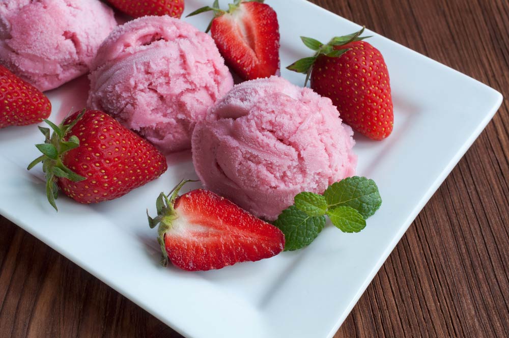 Полуничне морозиво з цілими і розрізаними ягодами полуниці та м'ятою на білій тарілці