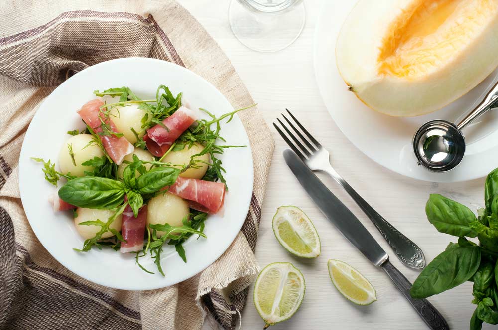 Салат з кульками дині, шинкою та руколою на білому столі