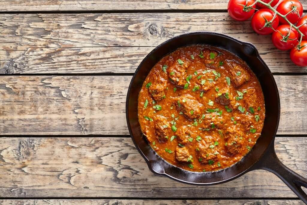 Гуляш із яловичини в сковороді на дерев’яному столі поруч із помідорами