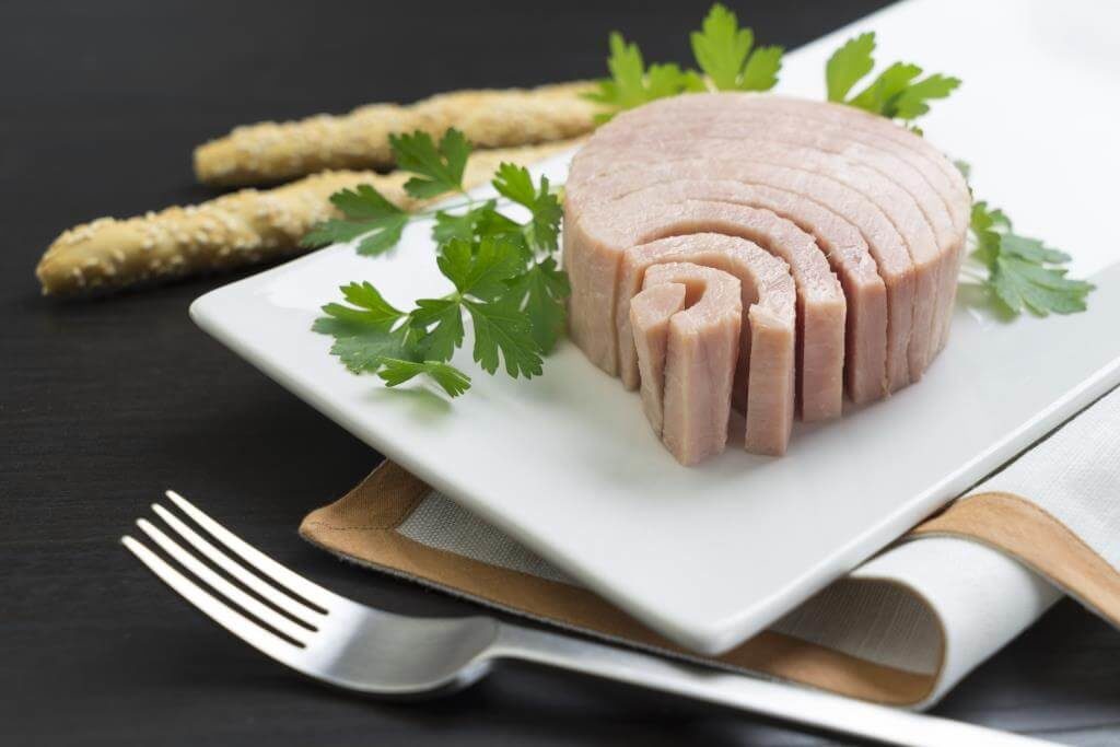 Слайсований тунець на тарілці з петрушкою та грісіні на чорному фоні