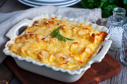 Запечена картопля з сиром у керамічній формі, прикрашена гілочкою кропу