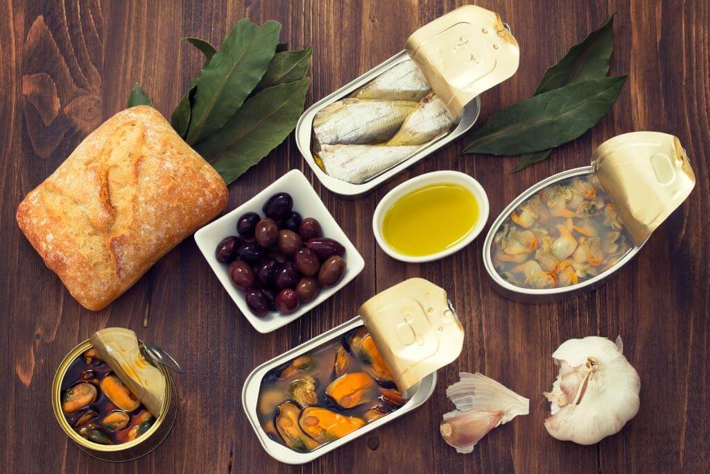 Набір морепродуктових консервів із хлібом, оливками, часником, лавровим листям та олією.