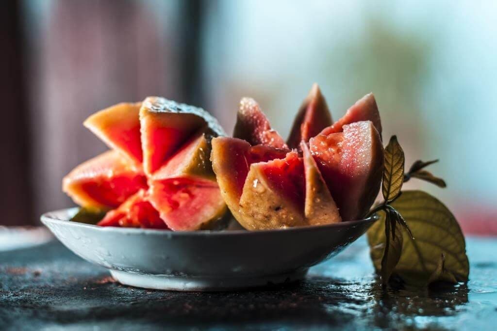 Нарізані шматочки рожевої гуави на тарілці з листочком, крупним планом на тлі розмитого фону