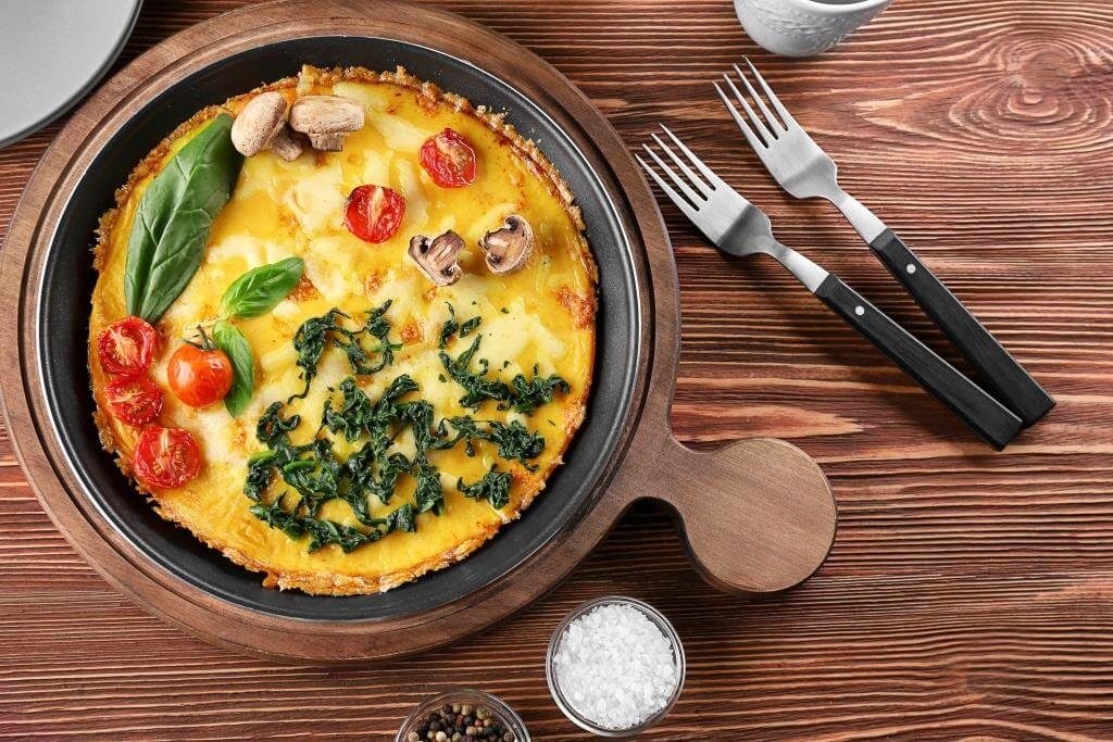 Омлет з овочами — помідорами чері, грибами та шпинатом на сковороді